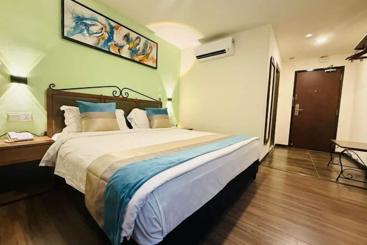 A hotel room with a bed, nightstand, wall art, air conditioning unit, and a door.