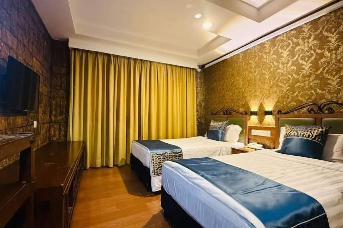A hotel room with two beds, a desk, a TV, and a large window with curtains.