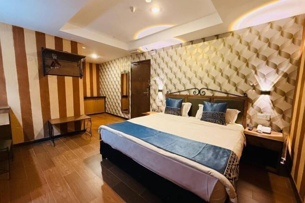 A hotel room with a large bed, a desk, a TV mounted on the wall, and a patterned wall.