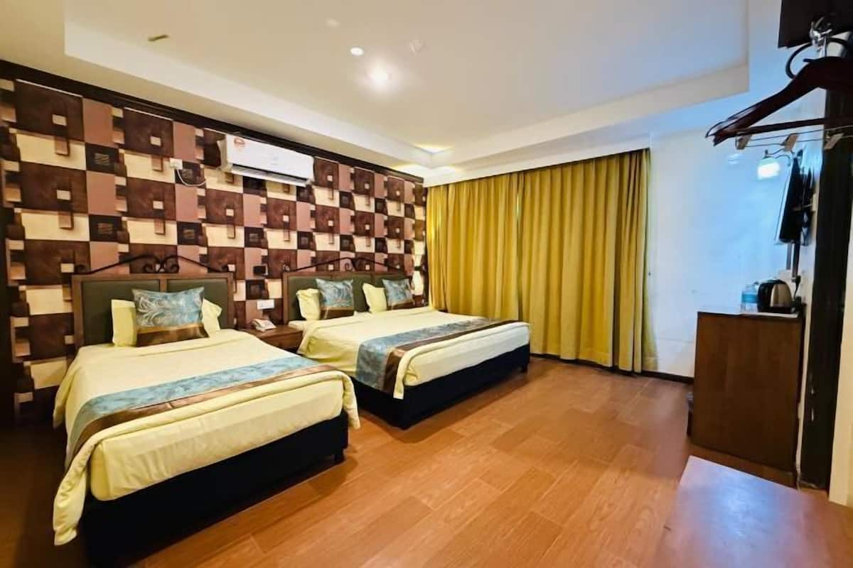 A hotel room with two beds, a wooden floor, a wall-mounted TV, and a wardrobe.