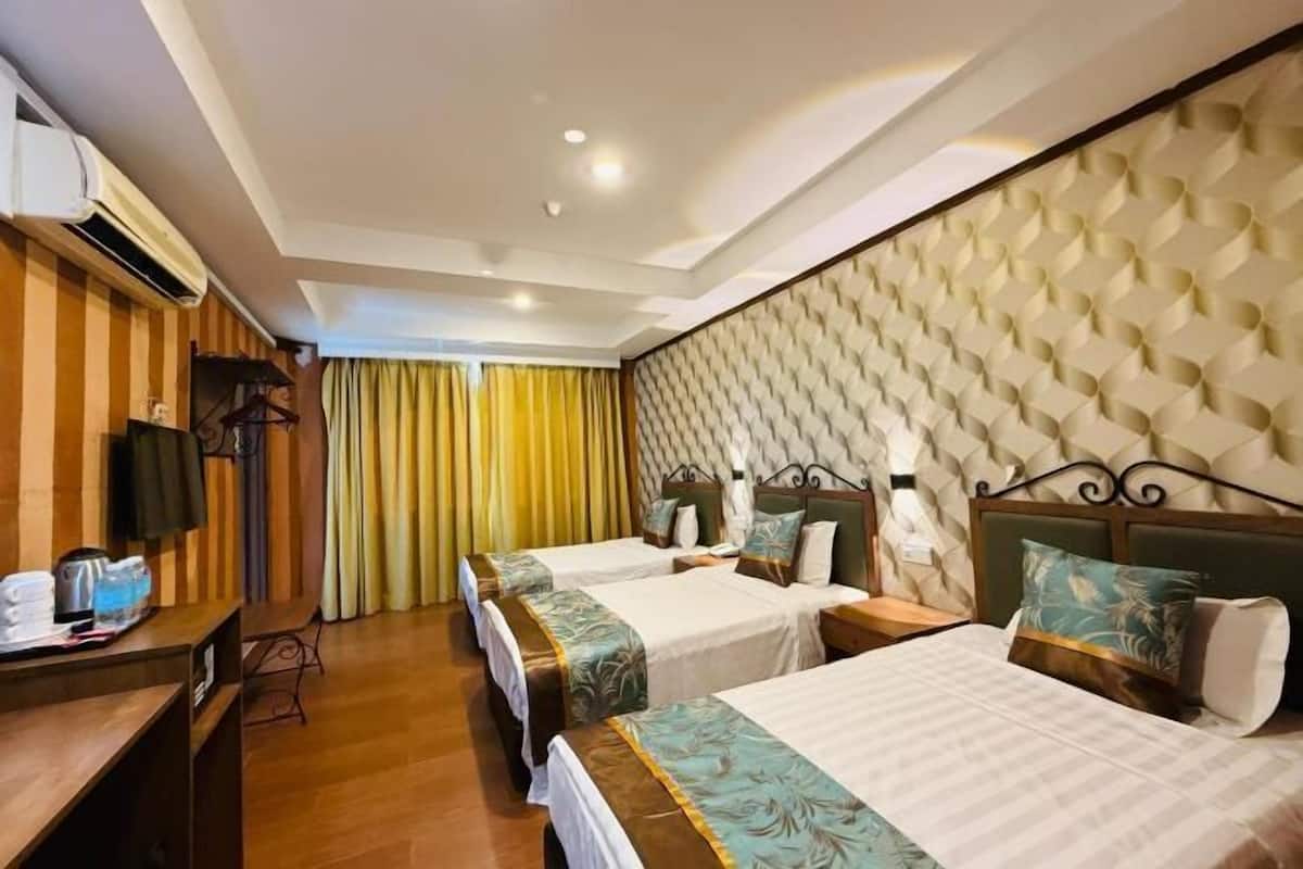 A hotel room with three beds, a desk, a television, and a window with curtains.