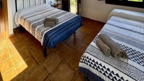 Ein Schlafzimmer mit zwei Betten, Holzboden, einer Deckenleuchte und einem Fenster mit Blick ins Grüne.