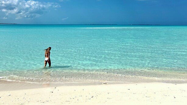 Une plage avec une eau turquoise et limpide, et une personne qui se promène dans les eaux peu profondes.