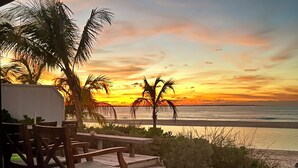 Une terrasse en bois avec des chaises, donnant sur une plage au coucher du soleil.