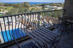 A balcony with a view of a swimming pool, outdoor furniture, and a distant landscape. - The Figolla Farmhouse - Gizimina 1 (Ix-Xagħra)
