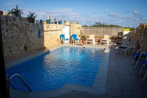 A swimming pool with a stone wall, blue chairs, and potted plants. - The Figolla Farmhouse - Gizimina 1 (Ix-Xagħra)