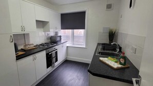 Una cocina compacta con gabinetes blancos, cocina a gas, microondas y fregadero.