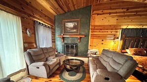 L’intérieur d’un chalet accueillant, avec deux canapés, une table basse, une cheminée et un lit recouvert d’une couvre-lit à motifs.