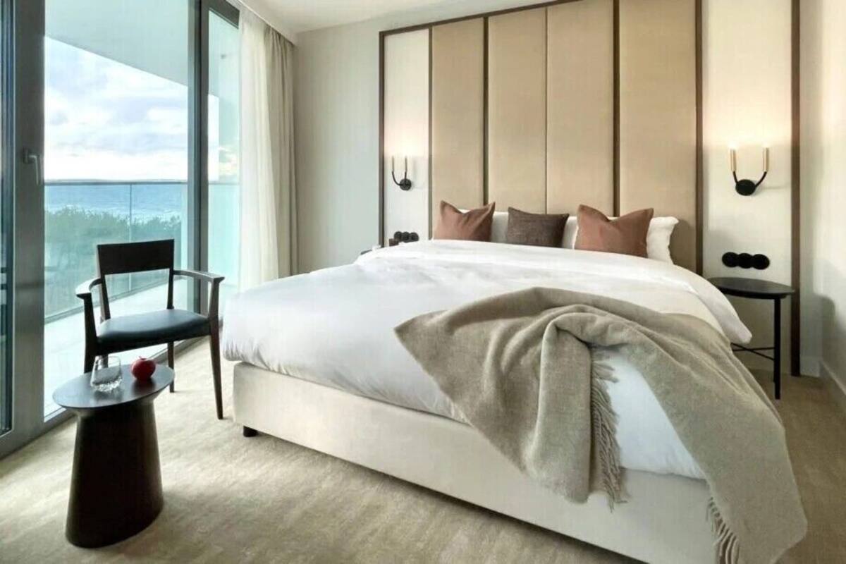 Ein modernes Hotelzimmer mit einem großen Bett, einem Sessel, einem kleinen Tisch und Blick ins Freie.