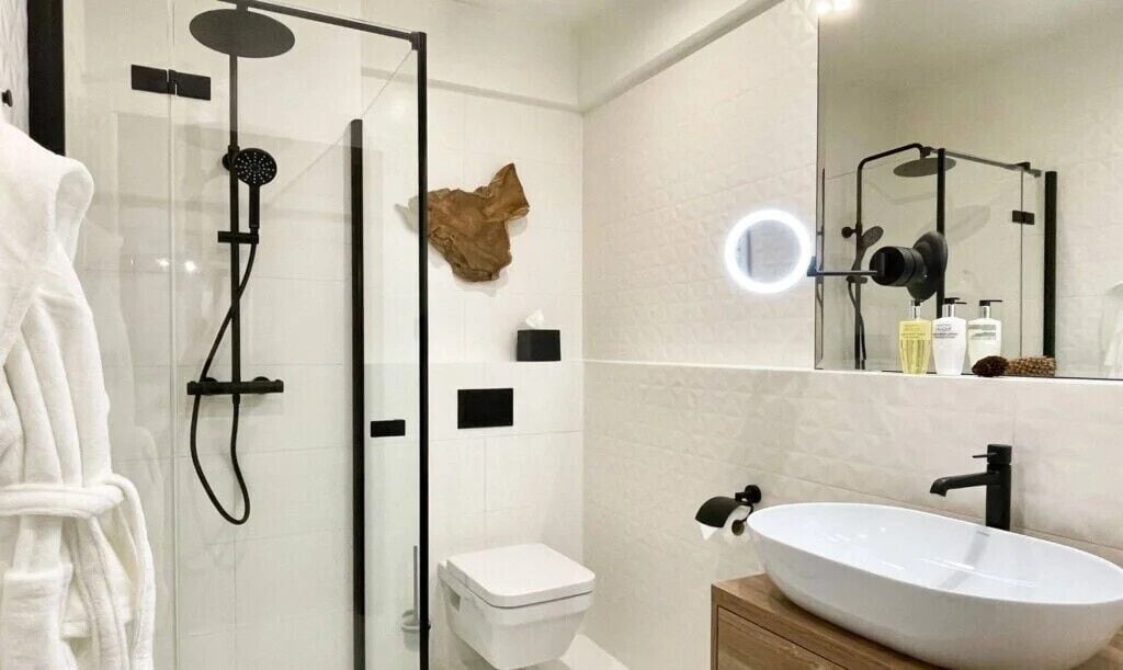 Een moderne badkamer met een douchecabine van glas, een wit toilet en een groot ovaal wastafel met een spiegel erboven.