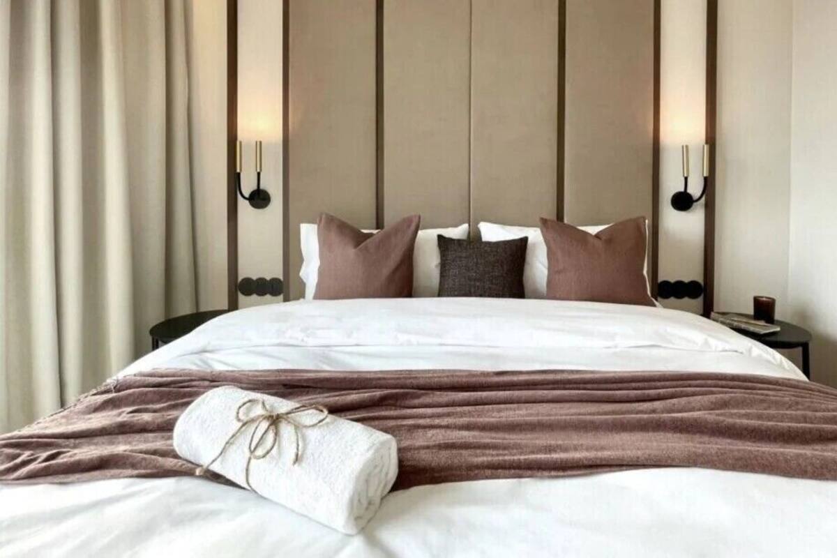 Ein Hotelzimmer mit einem großen Bett, einer Kopfteil mit vertikalen Paneelen, zwei Wandlampen und einem Nachttisch mit Lampe.
