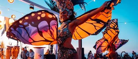A person in a butterfly costume with wings, standing in an outdoor setting with a stage and musical equipment in the background.