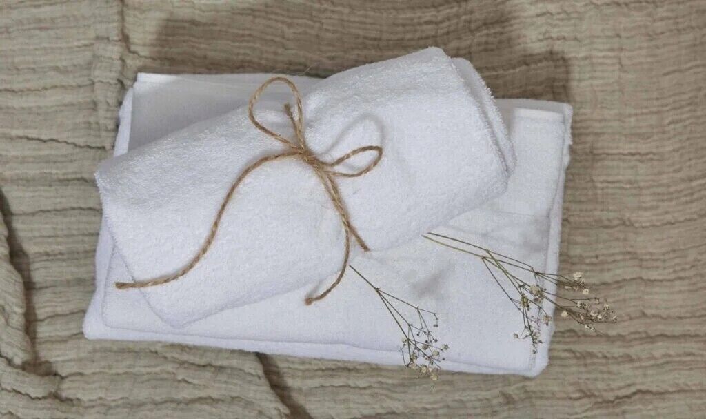 A white towel tied with twine on a white plate, with small dried flowers beside it.