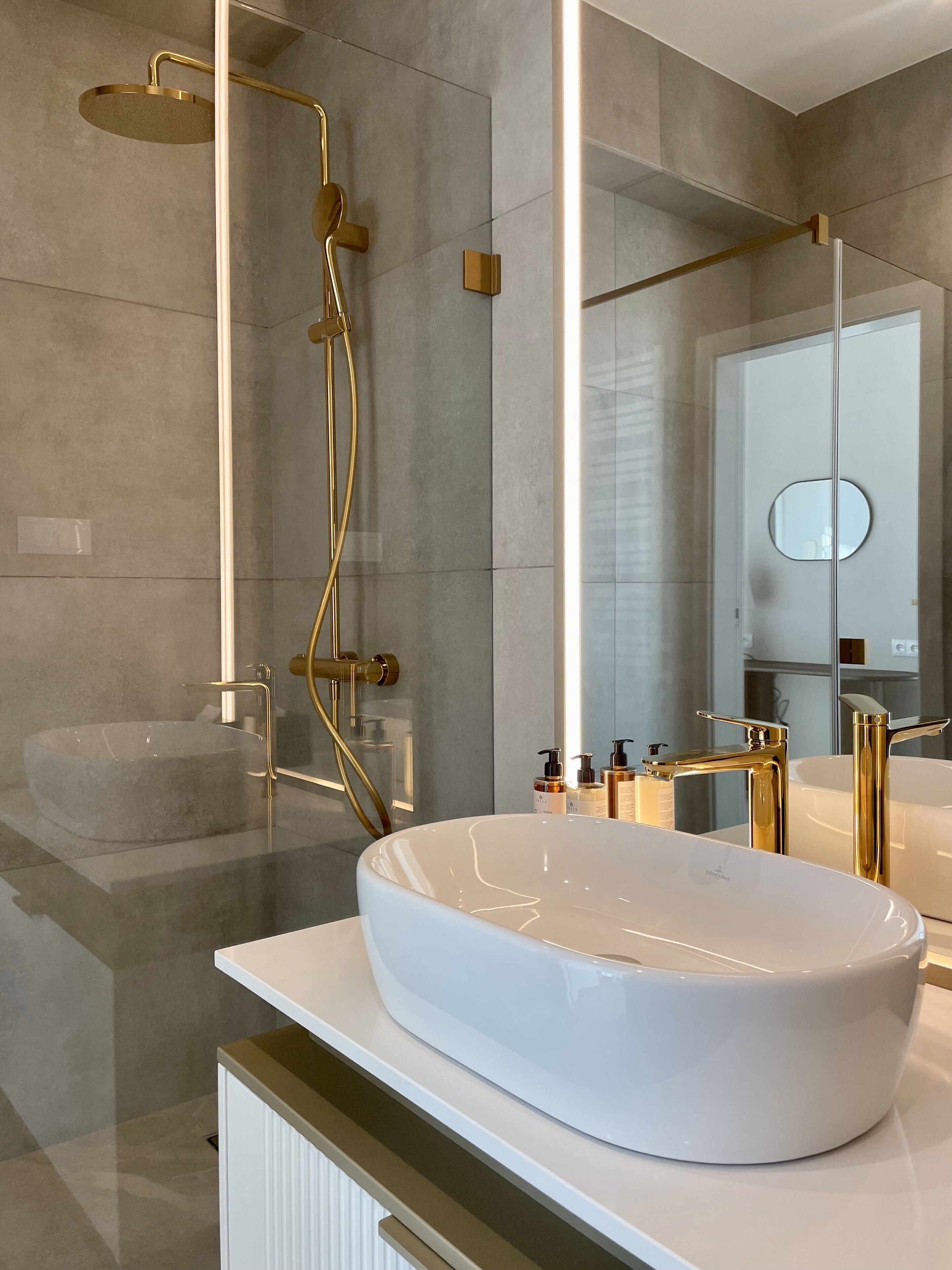 A modern bathroom with a large oval sink, gold fixtures, and a glass-enclosed shower.