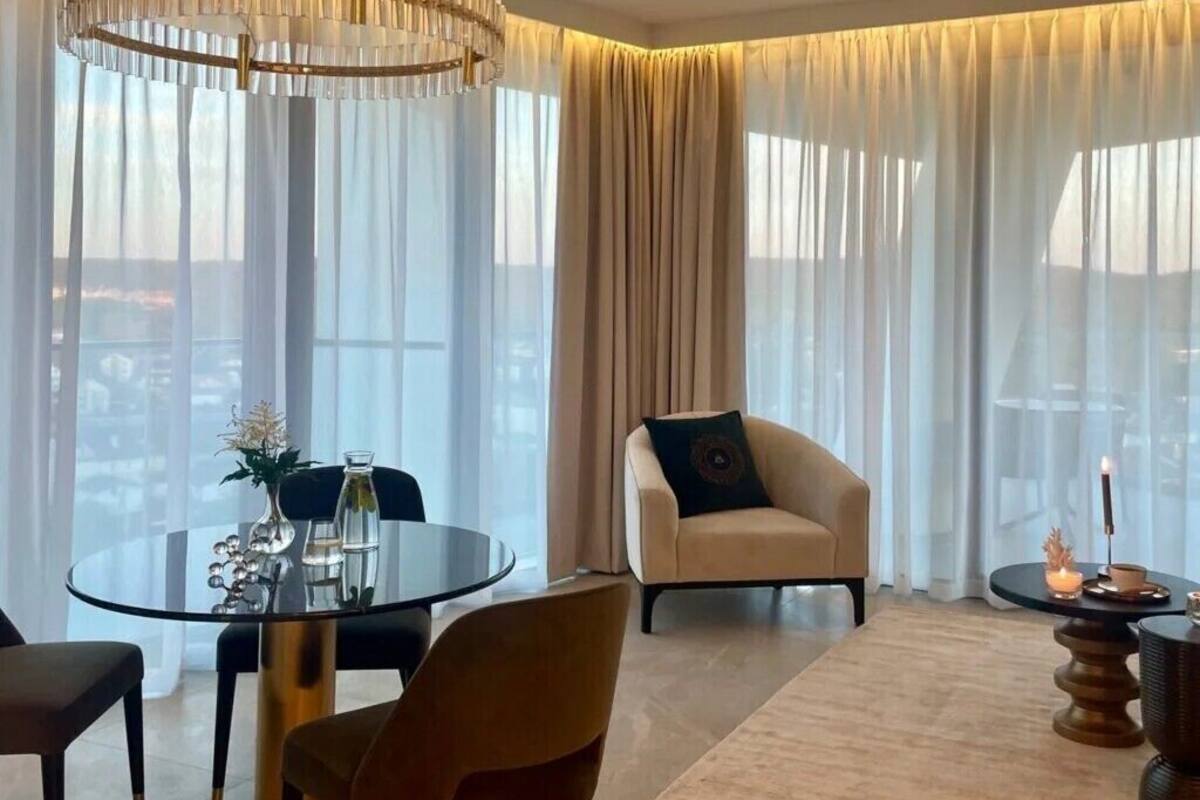 Ein modernes Hotelzimmer mit einem runden Esstisch, einem bequemen Sessel und einem großen Fenster mit leichtem Vorhang.