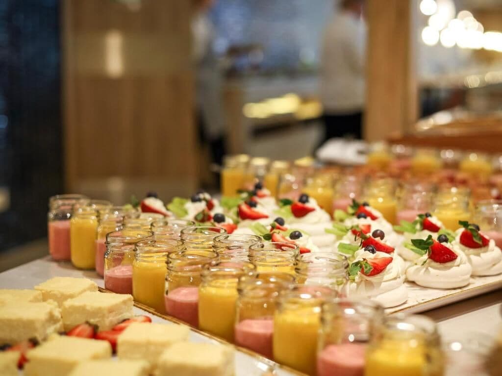 A buffet with various desserts including meringues, fruit tarts, and custard in jars.