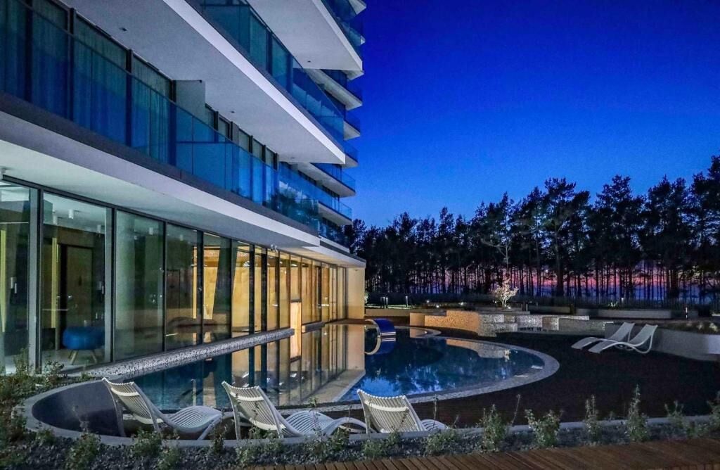 Un hôtel moderne doté d’un espace piscine sur le toit, comprenant des chaises longues et une piscine protégée par des parois en verre.