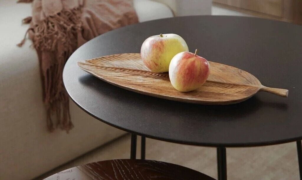 Ein runder Tisch mit einer tellerförmigen Holzplatte, auf der zwei Äpfel liegen.