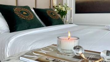 A neatly made bed with two pillows, a magazine, and a lit candle on a marble table.