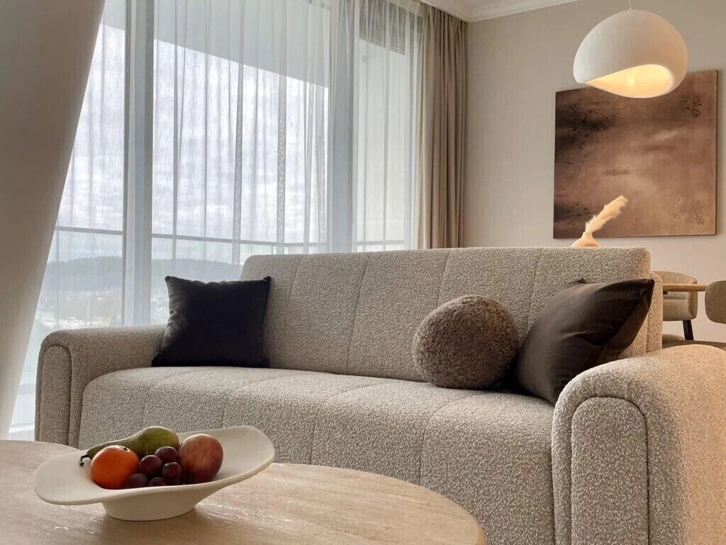 Ein modernes Wohnzimmer mit einem grauen Sofa, einem runden Couchtisch und einer Obstschale.
