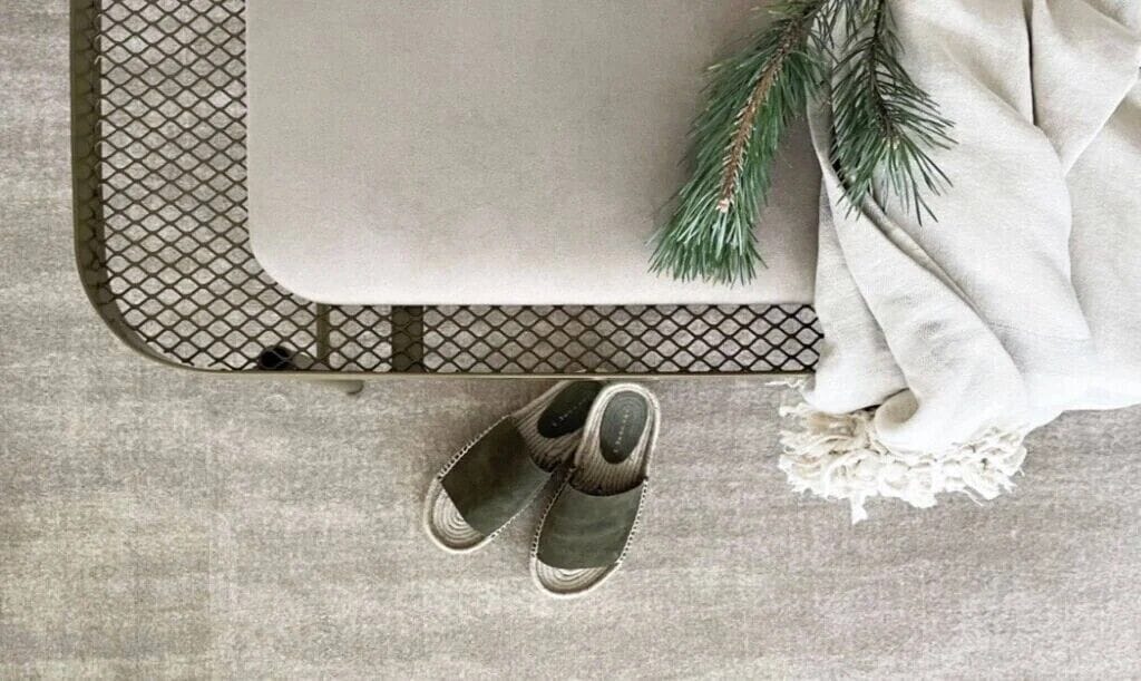 A pair of green slippers, a white cloth, and a pine branch on a textured surface.