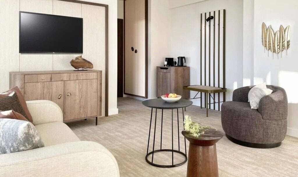 A modern living room with a sofa, a round coffee table, a grey armchair, a TV mounted on the wall, a cabinet, and a decorative wall piece.