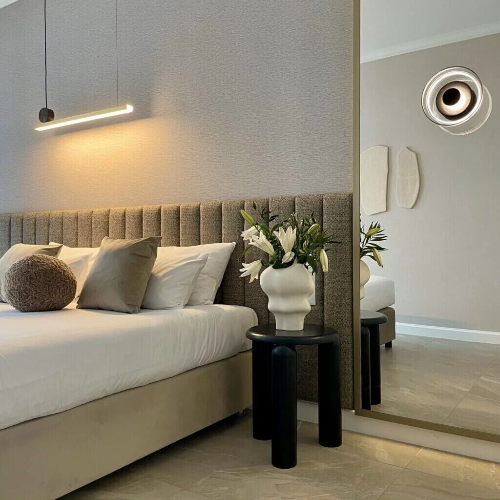 A modern bedroom with a bed, bedside tables, a vase with flowers, and a mirror.