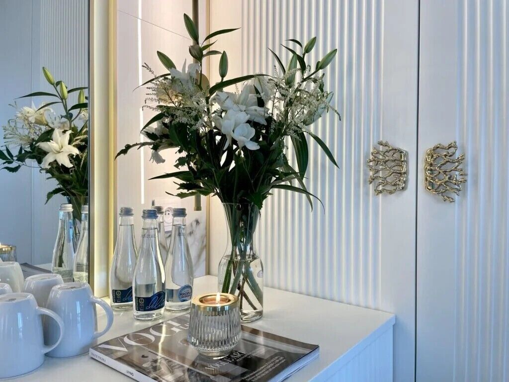 A bathroom vanity with a white marble countertop, a magazine, and a vase of white flowers.