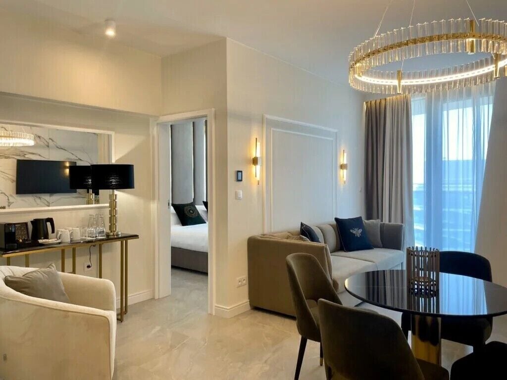 Une chambre d’hôtel moderne comprenant un coin repas, un ensemble de canapés, un téléviseur et un lustre.