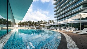 A modern hotel pool area with a clear blue pool, sun loungers, umbrellas, and a multi-story building in the background. - Wave Międzyzdroje Resort & Spa (Międzyzdroje)