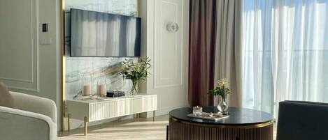 A modern living room with a round coffee table, a sofa, a TV mounted on a marble wall, and a large window with curtains.