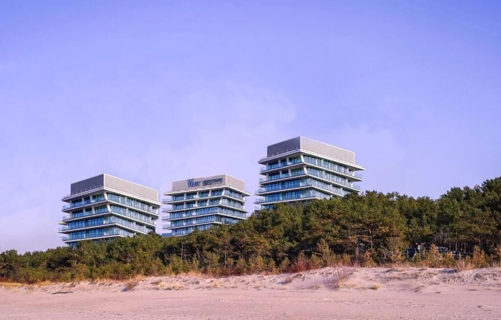 Un hotel moderno con tres edificios conectados, rodeado de un bosque denso.