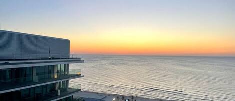 A modern building with multiple floors overlooking a beach at sunset.
