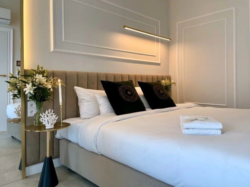 A modern hotel room with a large bed, a bedside table with a vase of flowers, and a wall-mounted light fixture.