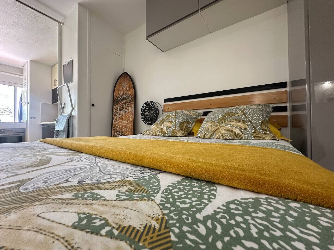 A bedroom with a bed, a headboard, a wall-mounted shelf, and a door.