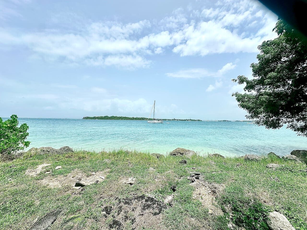 Eine Küstenlandschaft mit freiem Blick auf das Meer, einer entfernten Insel und einem Segelboot.