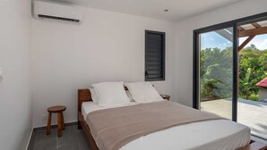 A bedroom with a bed, a window, a small stool, and a ceiling fan.
