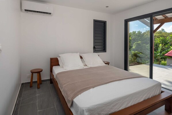 Un dormitorio con cama, ventana, un taburete pequeño y ventilador de techo.