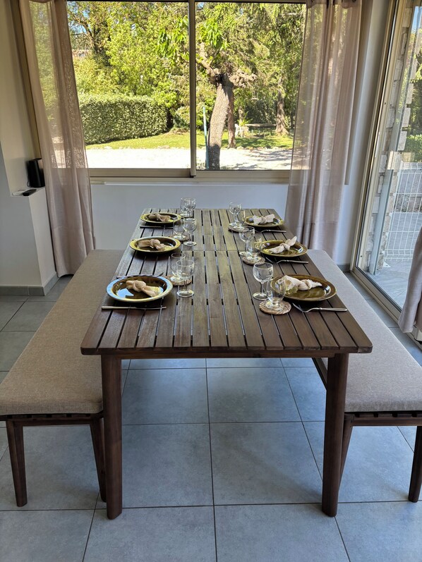 A dining table set for six with plates, glasses, and cutlery, positioned in a room with a view of greenery outside. - Villa Campagne Aixoise (fuveau)