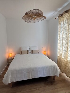 Un dormitorio con cama, dos lámparas de noche, una lámpara colgante y una ventana con cortinas.