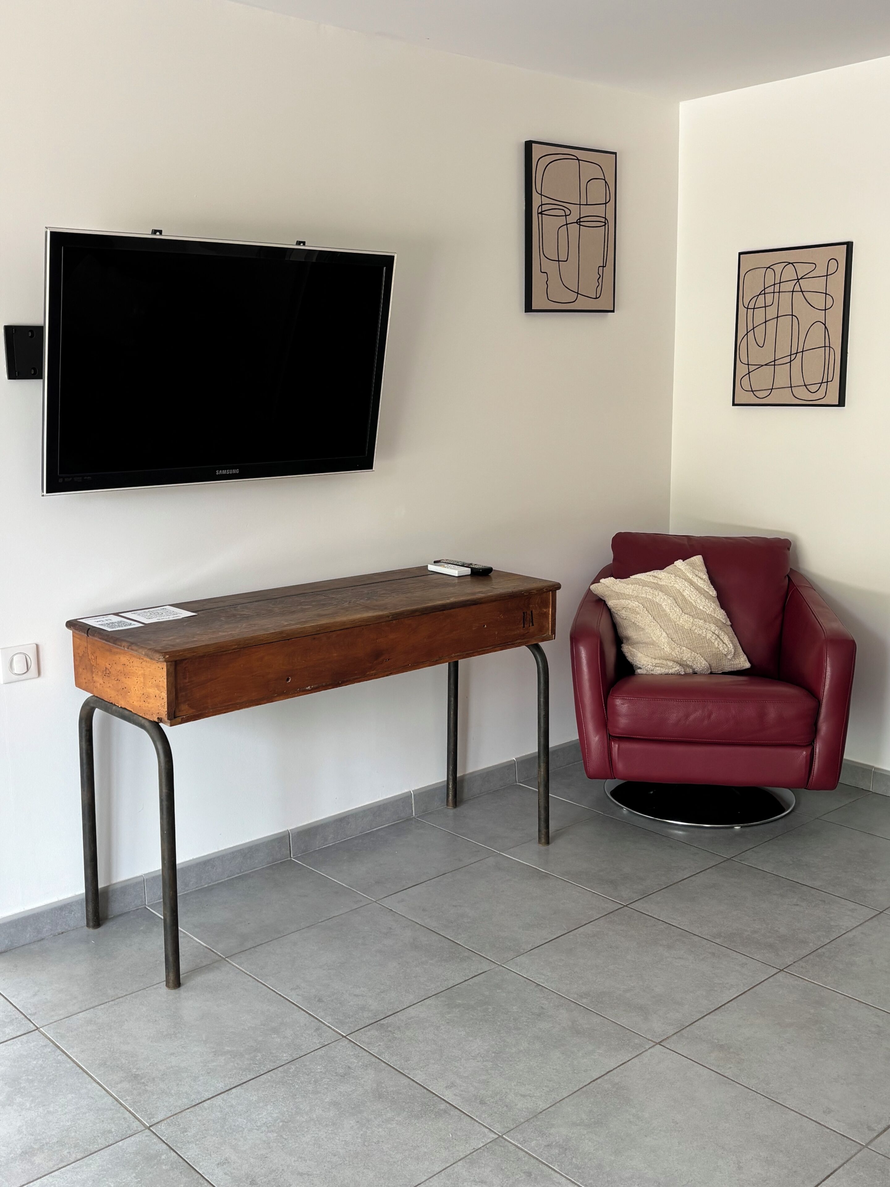 Ein modernes Wohnzimmer mit Flachbildfernseher, einem Holztisch, einem roten Ledersessel und zwei abstrakten Wandbildern.
