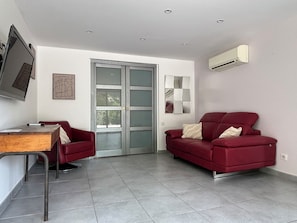 Una sala de estar moderna con un sofá rojo, una mesa de madera, un televisor montado en la pared y un ventanal corredero.