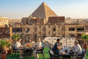 A rooftop dining area with a view of the pyramid, surrounded by buildings. - Families Pyramids view - Rooftop (Nazlet Al Batran)