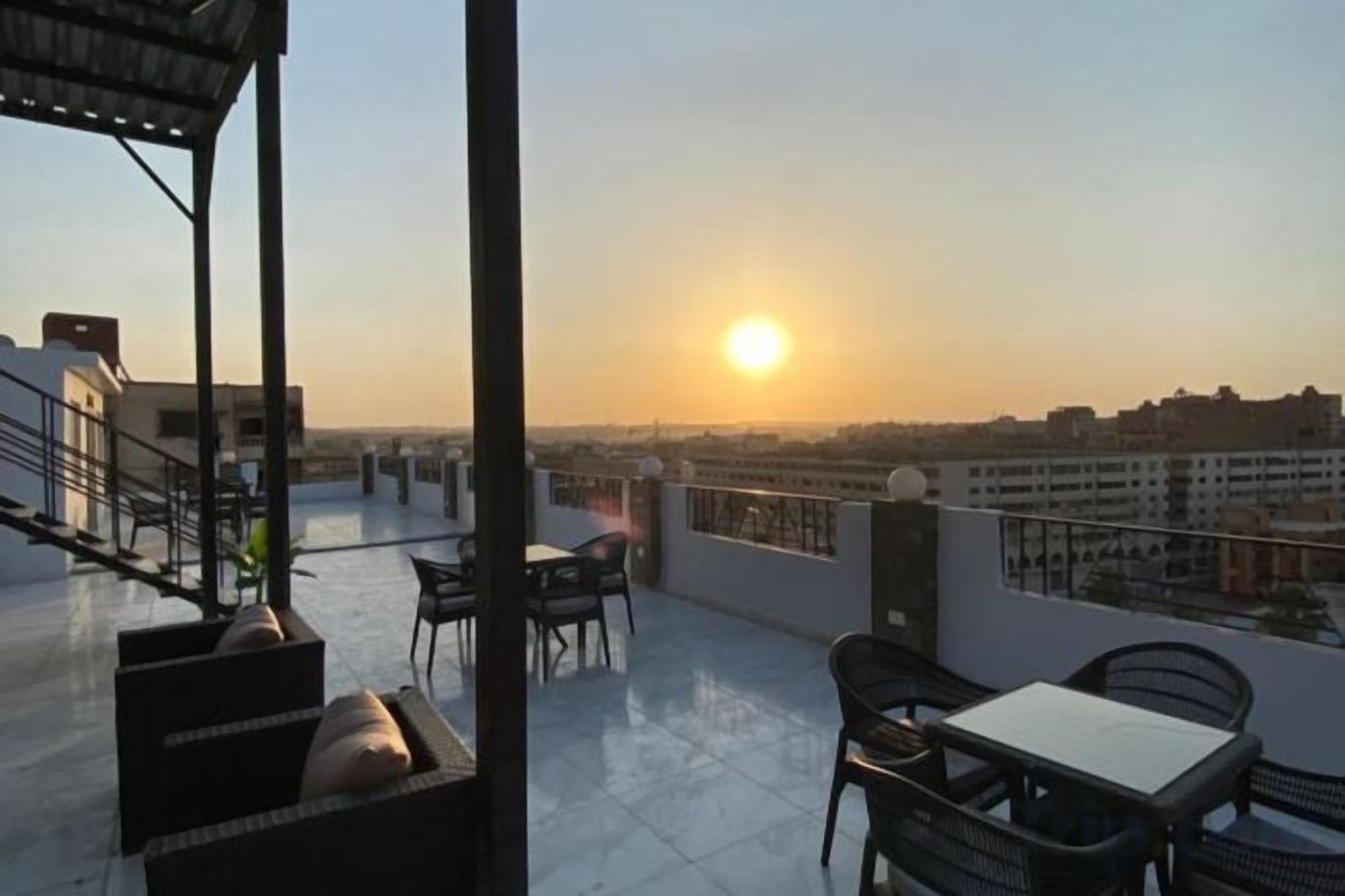 A rooftop terrace with a view of the sunset, outdoor seating, and a railing.