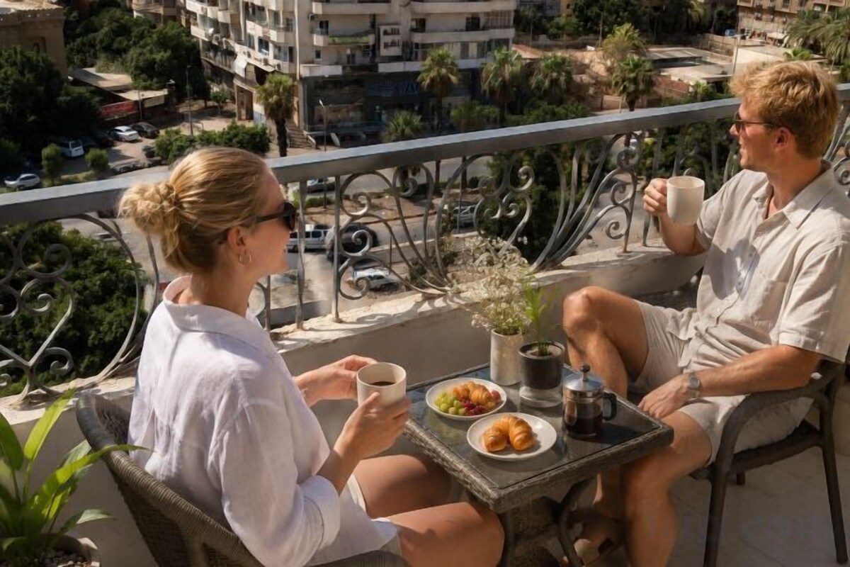 Two people seated at an outdoor table with a view of the cityscape, a coffee cup, and a plate of food.
