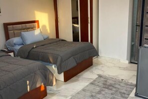 Une chambre d’hôtel avec deux lits, une tête de lit en bois, un sol en marbre et une porte coulissante donnant accès à la salle de bain.