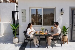Two people dining at an outdoor table with a city view, a potted plant, and a door in the background. - Families Pyramids view - Rooftop (Nazlet Al Batran)