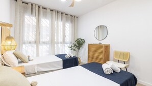 Une chambre d’hôtel avec deux lits, une table de chevet avec une lampe, un miroir, une chaise et une plante en pot.