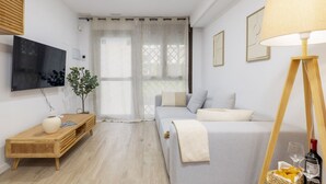 Un salon moderne avec un canapé, un téléviseur fixé au mur, une table d’appoint en bois et une lampe sur pied.