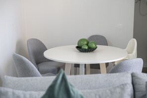 A round white table with a bowl of green apples in the center, surrounded by grey chairs.